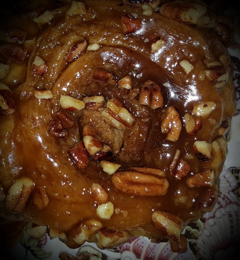 A pecan sticky bun under dark caramel glaze, pecan halves on top